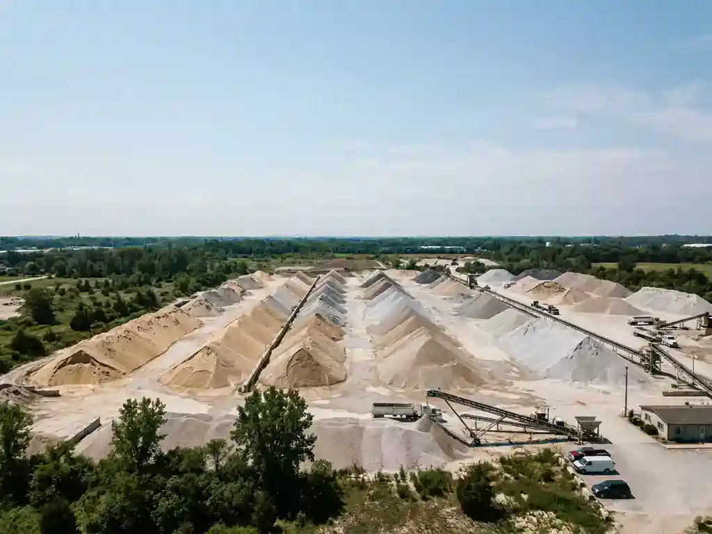 Luchtfoto van industrieel bulkopslagterrein met vochtige, stofvrije materiaalstapels in nette rijen onder heldere middagzon.